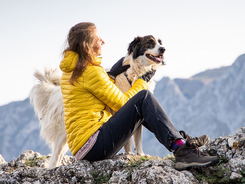 Donna seduta su roccia accarezza cane in montagna