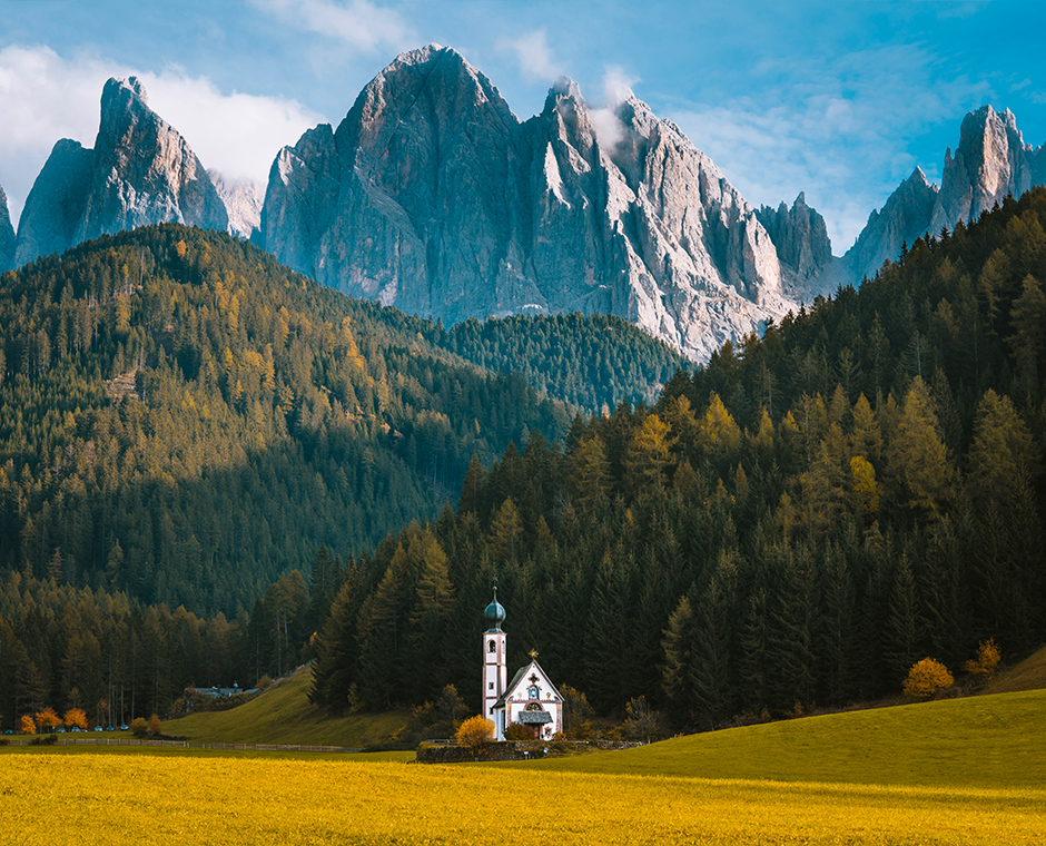 Chiesetta di San Giovanni in Ranui immersa nei prati verdi della Val di Funes con le maestose Odle sullo sfondo.