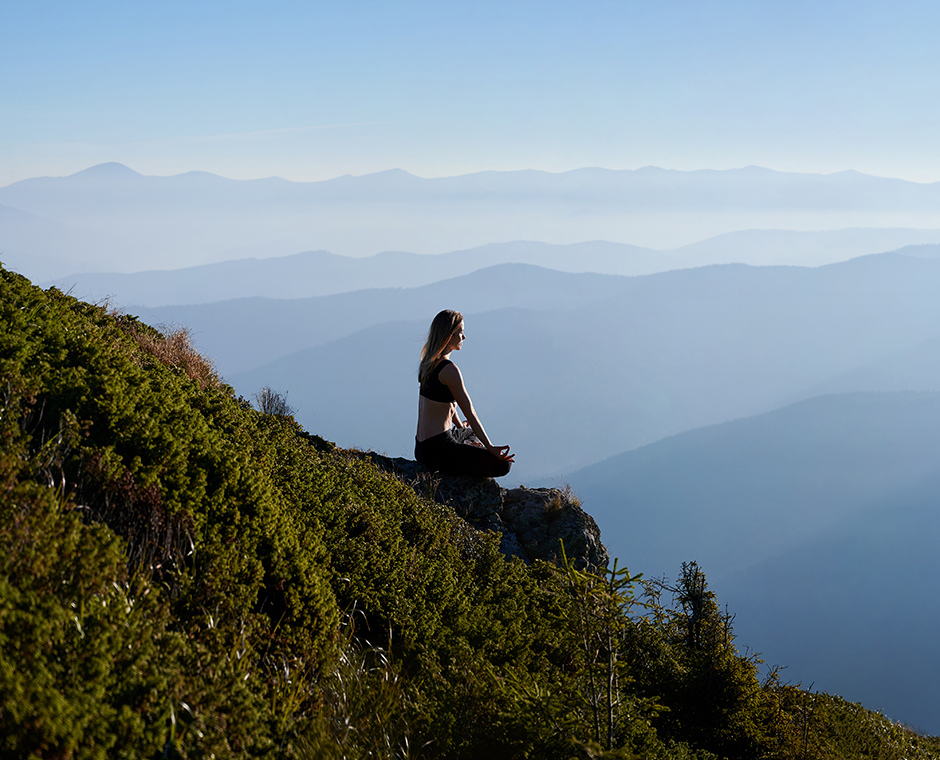 Donna in meditazione che si rilassa sull'erba in montagna.