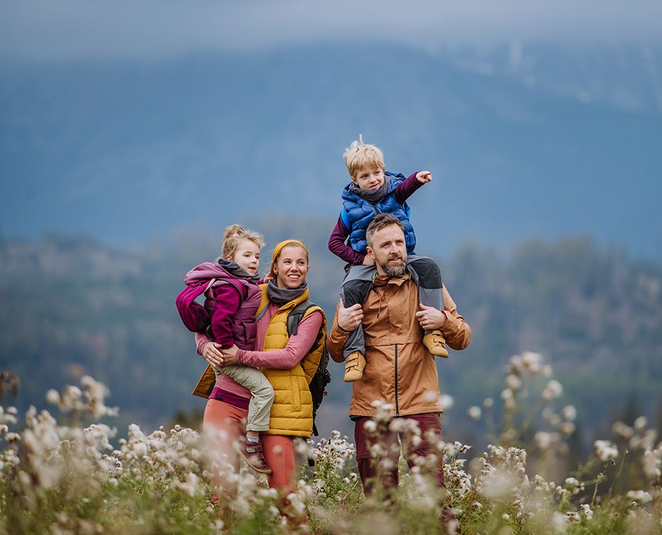 Genitori felici con i loro figli piccoli a cavalcioni durante una passeggiata autunnale, in mezzo alla natura colorata. Concetto di stile di vita sano. Trasporto dei bambini sulle spalle durante l'escursione.