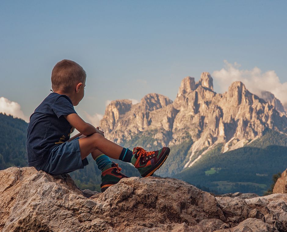 Un bambino su una roccia guarda il panorama delle Alpi