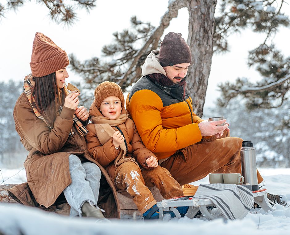 Famiglia felice con tazze di tè caldo che trascorre il tempo insieme nella foresta invernale, primo piano