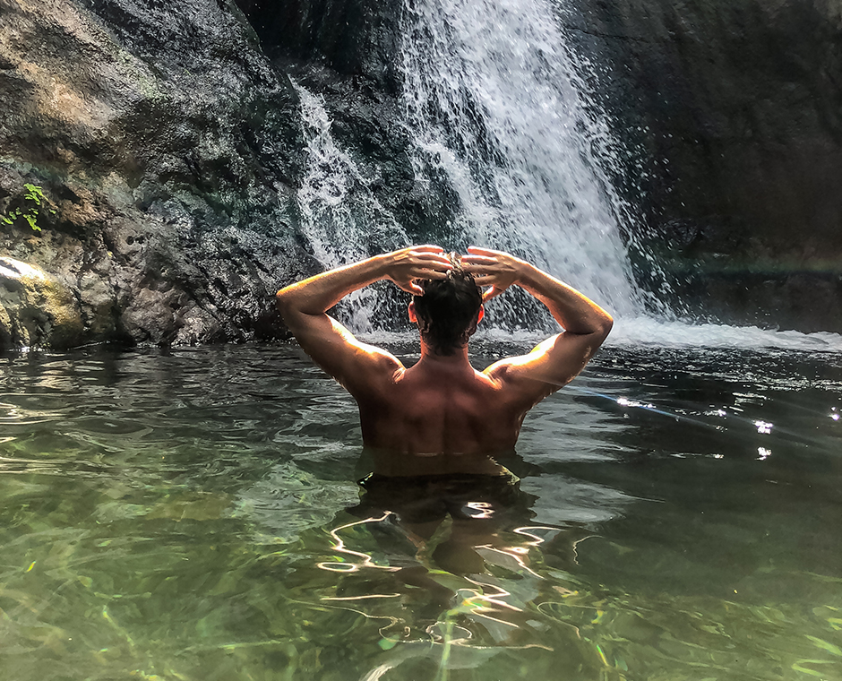 Vista posteriore di un uomo a torso nudo in piedi presso un lago con cascata