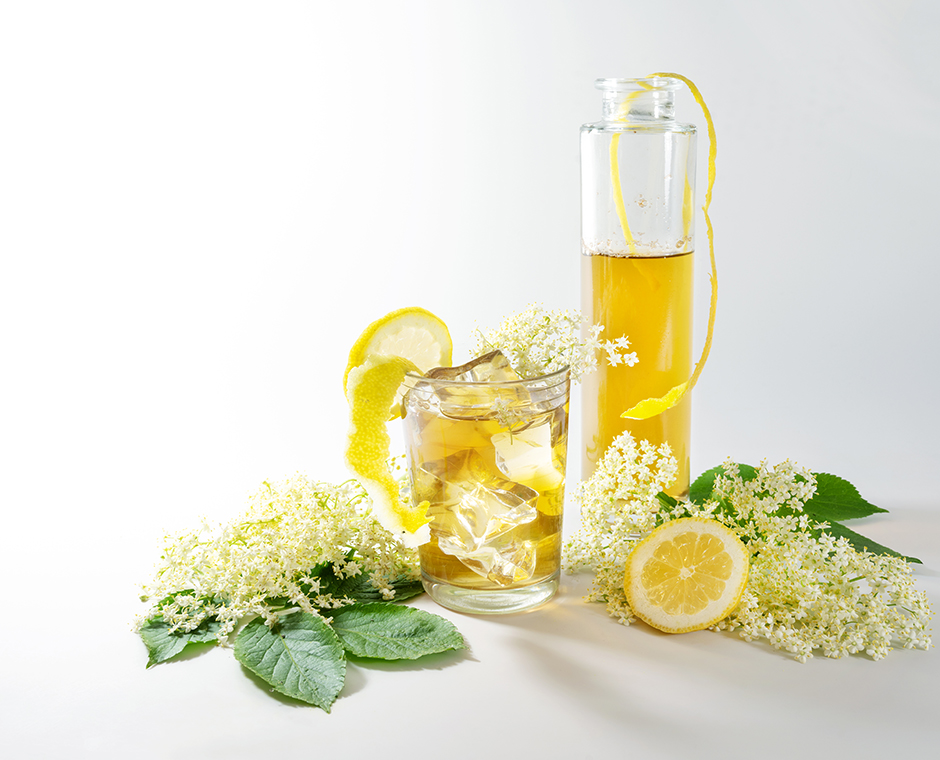 Sciroppo di fiori di sambuco in bottiglia e limonata fatta in casa con cubetti di ghiaccio in un bicchiere e fette di limone