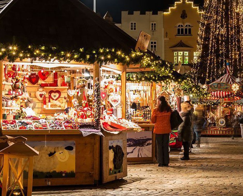Mercatino di Natale a Bressanone in Piazza Duomo, bancarelle intorno al duomo barocco e visitatori sulla piazza innevata