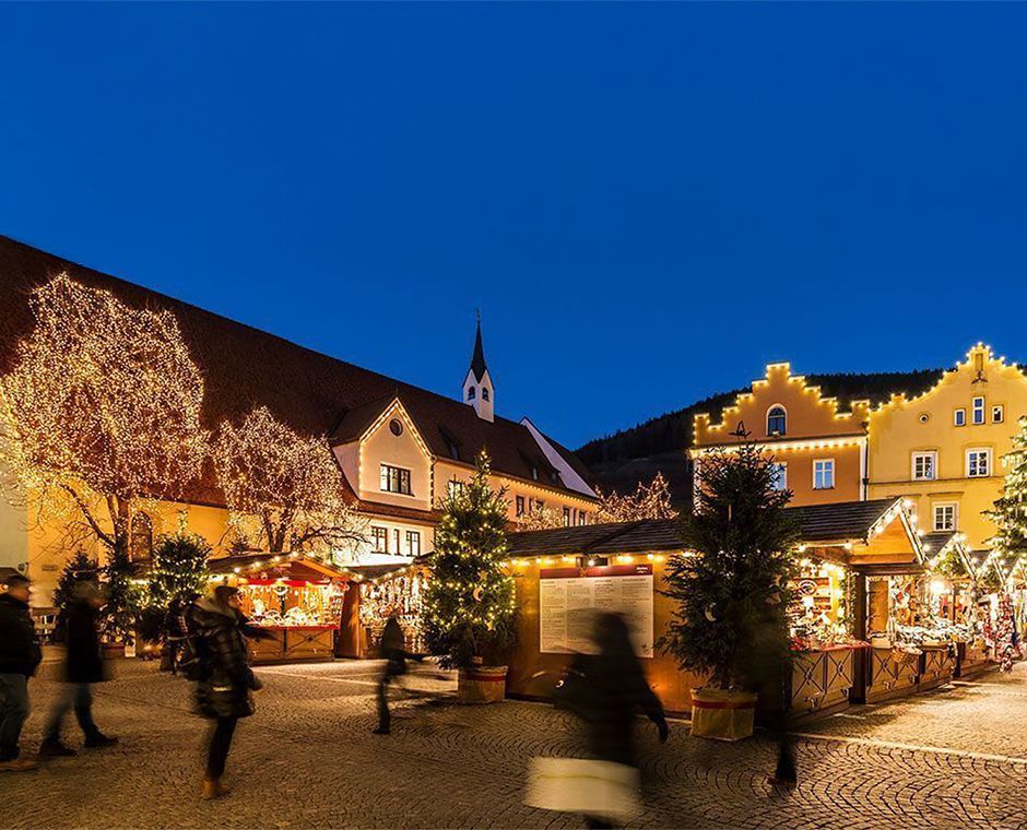Mercatino di Natale a Vipiteno con la Torre delle Dodici sullo sfondo, casette illuminate e atmosfera serale