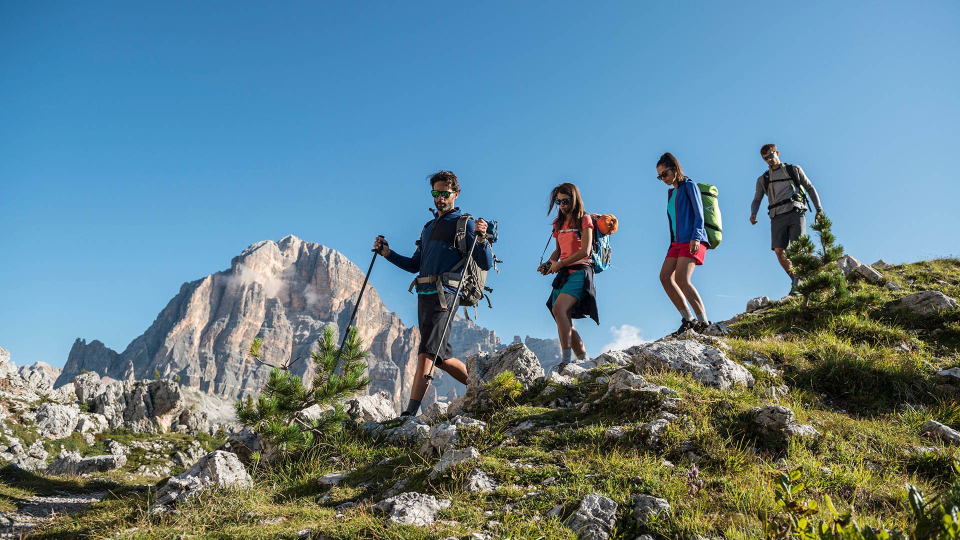 Gruppo di escursionisti cammina tra le rocce con vista sulle Dolomiti in una giornata estiva.