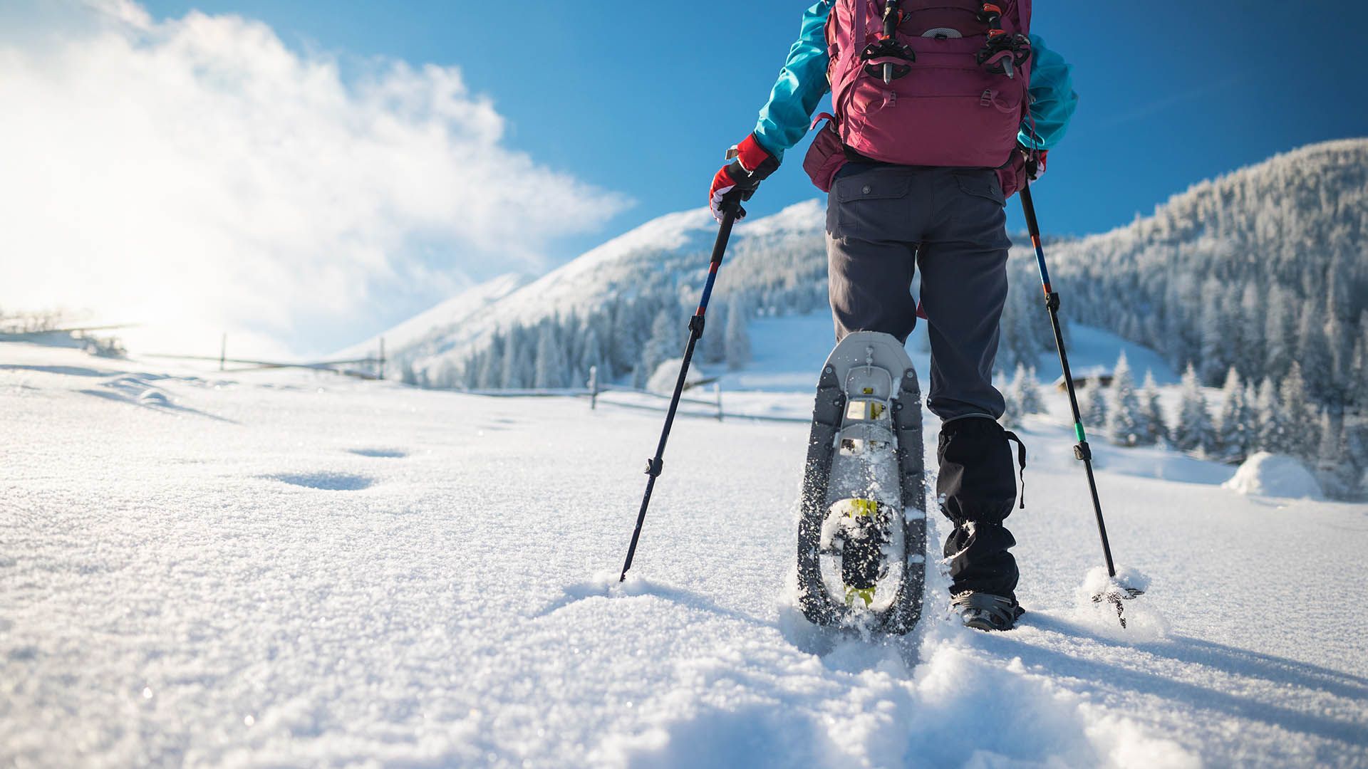 Escursionista con racchette da neve cammina su un sentiero innevato tra le montagne.