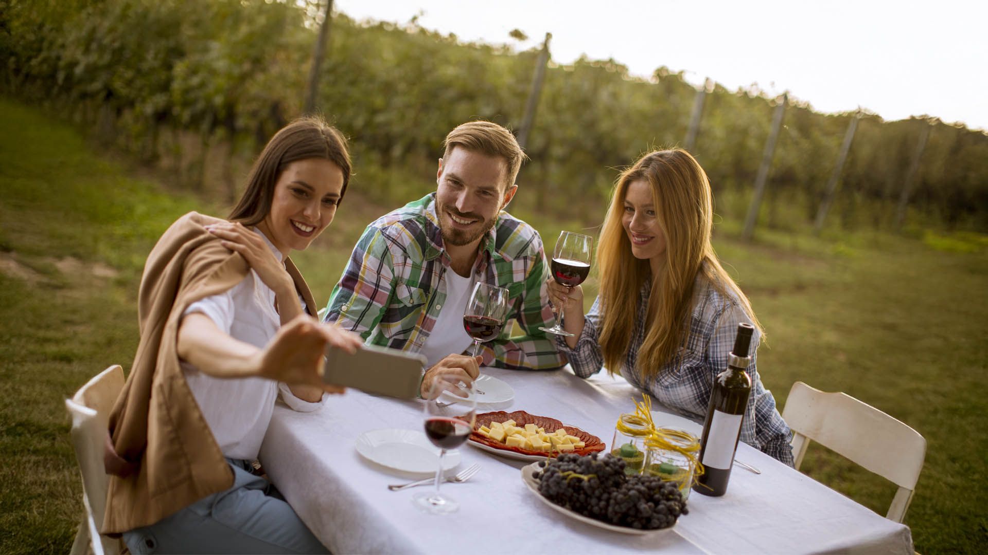 Tre amici brindano e fanno un selfie tra i vigneti.