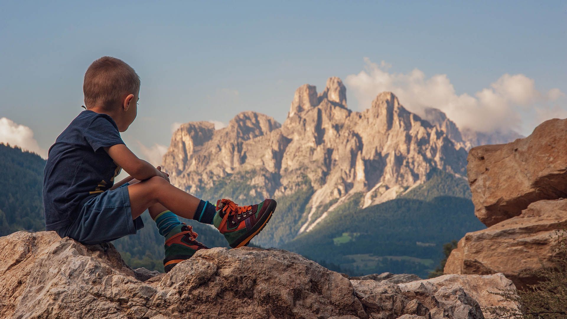 Bambino seduto su una roccia osserva le montagne durante un'escursione.