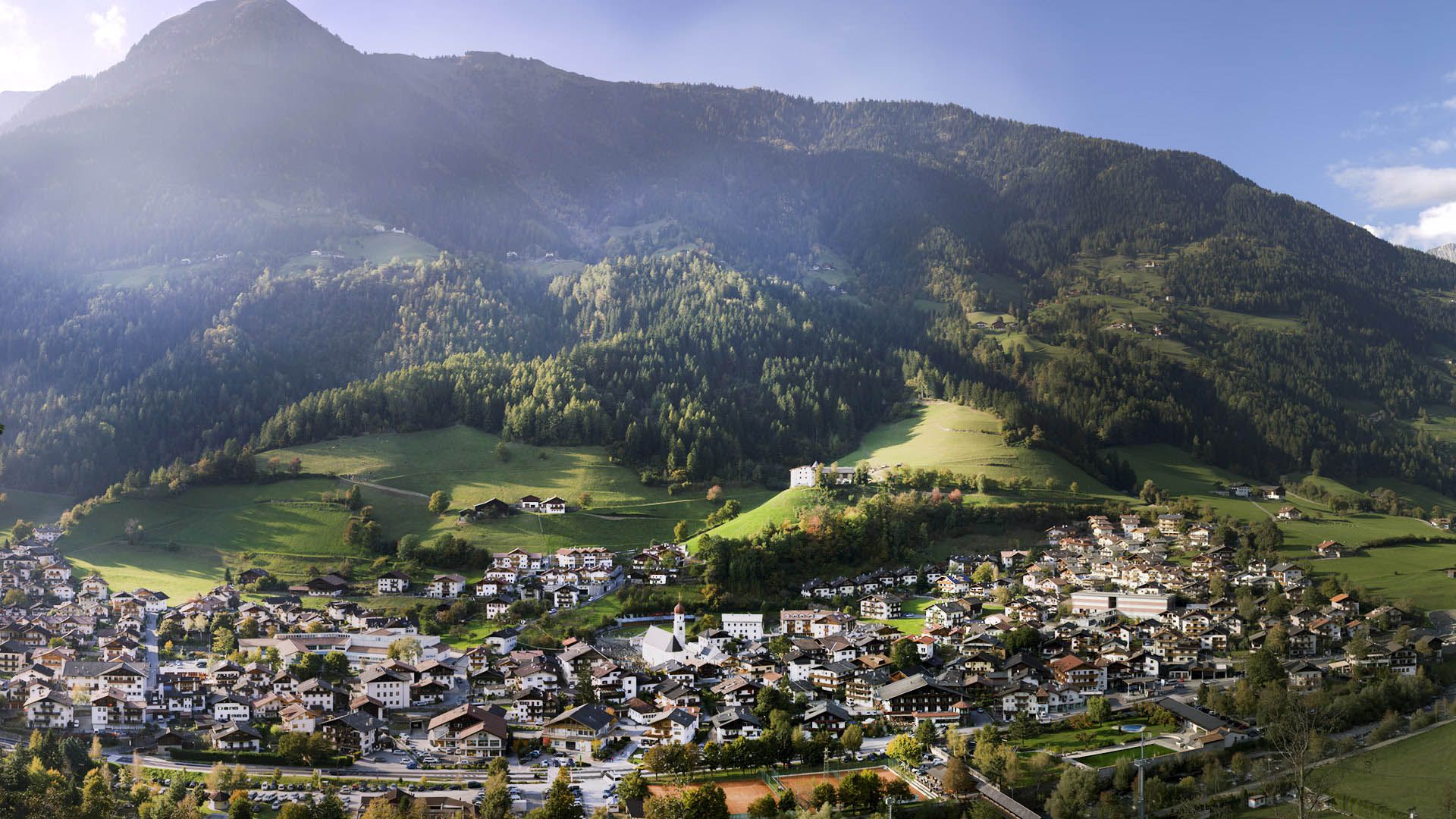 Panorama di San Martino in Passiria con chiesa, boschi e masi sulle pendici della valle