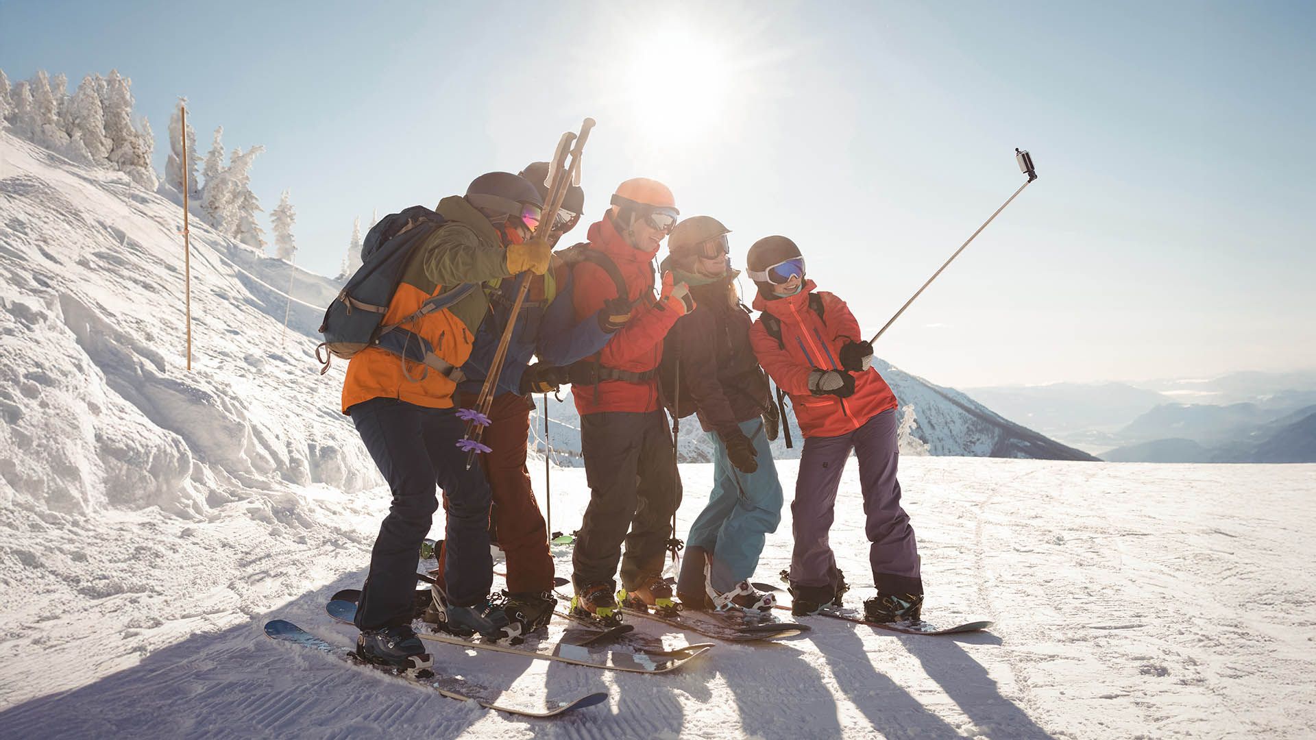 Gruppo di amici con sci e snowboard si scatta un selfie sulle piste innevate.