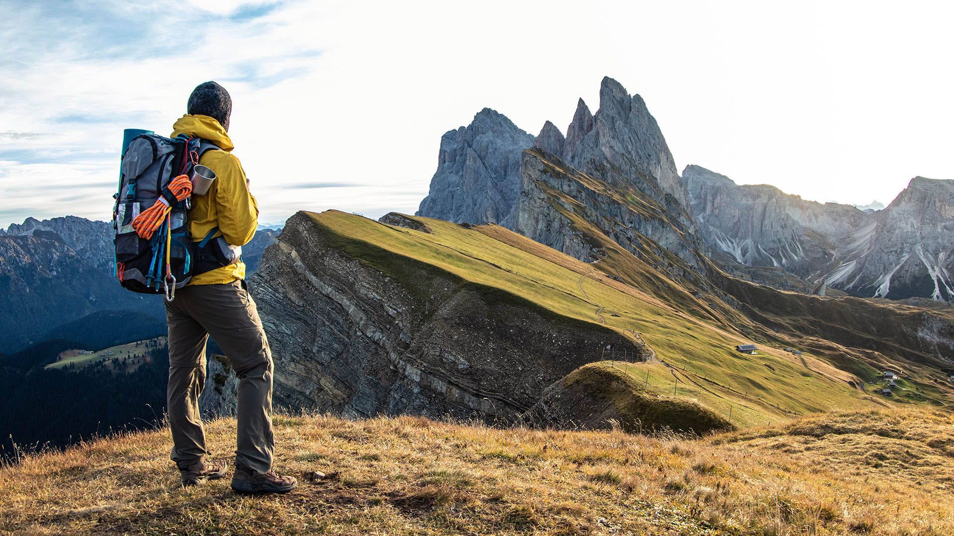 Escursionista su uno sperone roccioso osserva un lago alpino circondato da montagne.