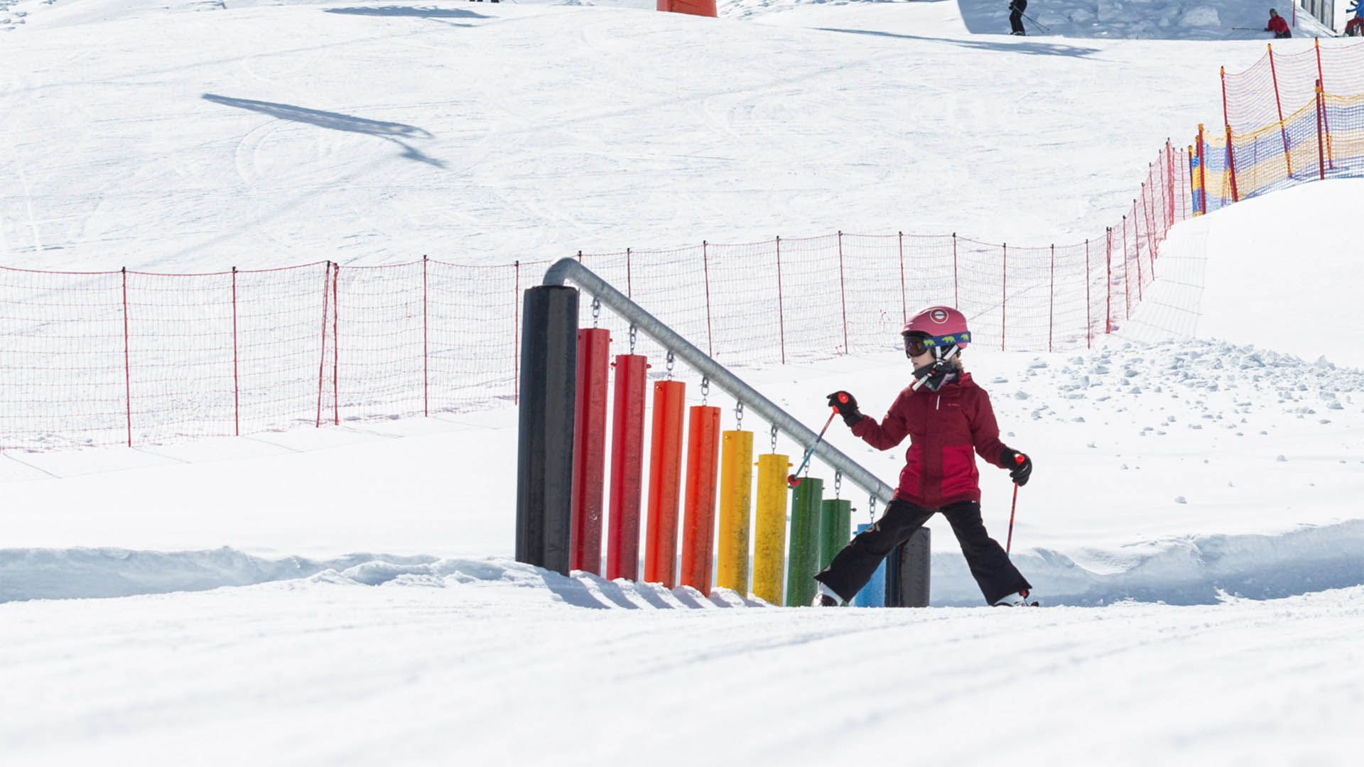 Bambino sugli sci vicino a xilofono colorato sulla neve, pista per bambini in Val Venosta