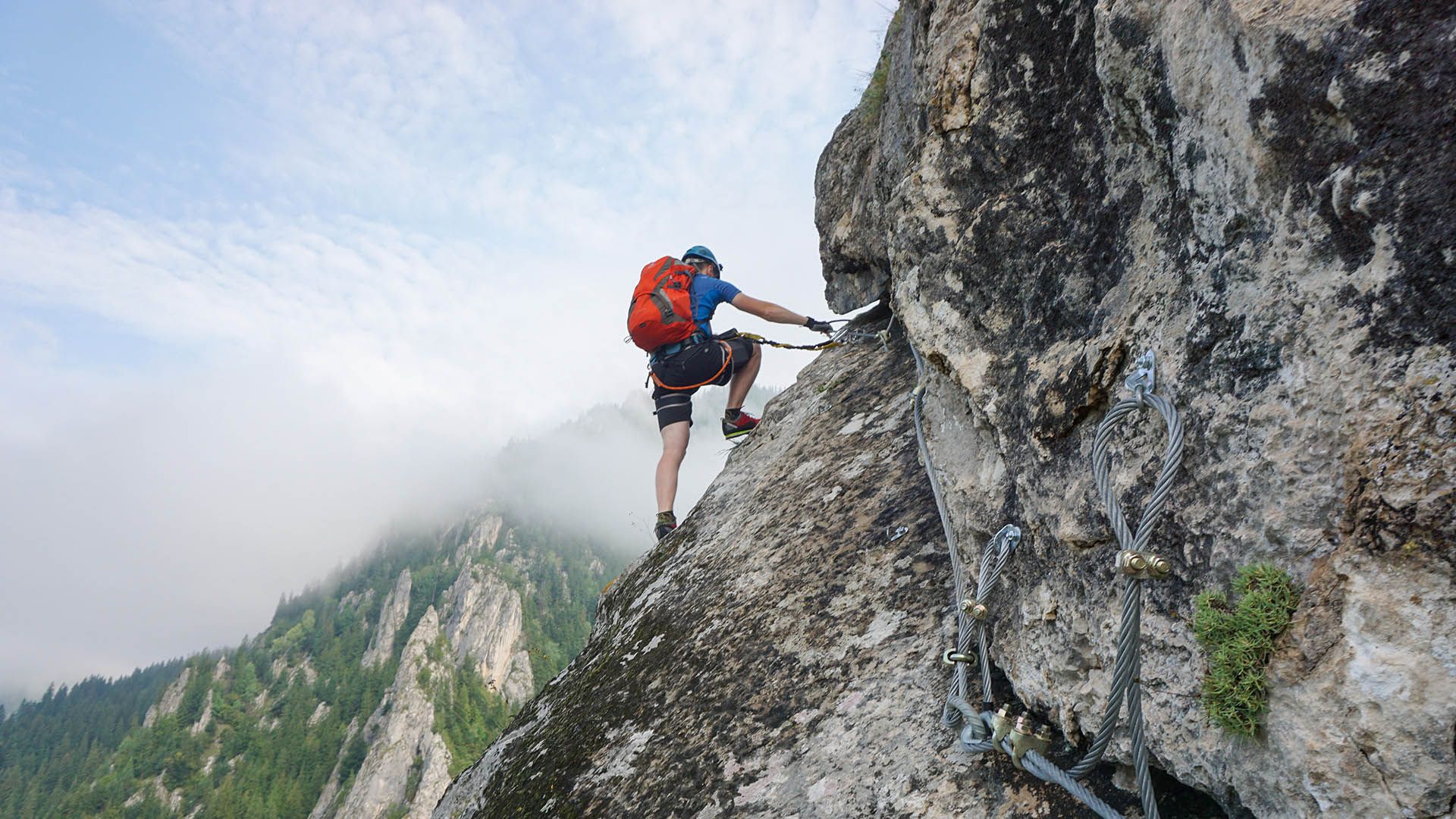 Alpinista su una via ferrata si arrampica assicurato con moschettoni e corde.