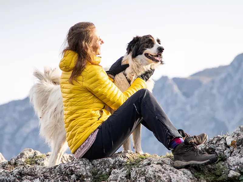 Donna seduta su roccia accarezza cane in montagna